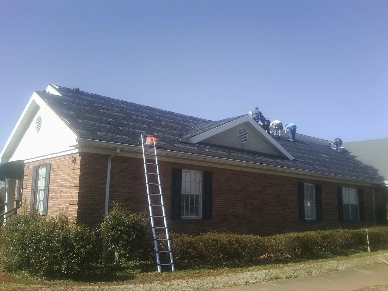 Crew tearing shingles off a brick ranch roof with a ladder set — Emergency Roof Repair work by our crew in West Berlin