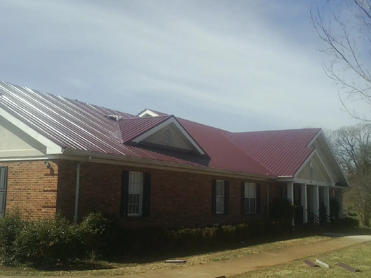 Red metal roof with gabled entries on a long brick building, from a Hail Damage Roof Repair job in West Berlin