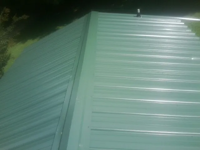 New green metal panels meeting at the ridge of a roof — Flat Roof Repair work by our crew in West Berlin
