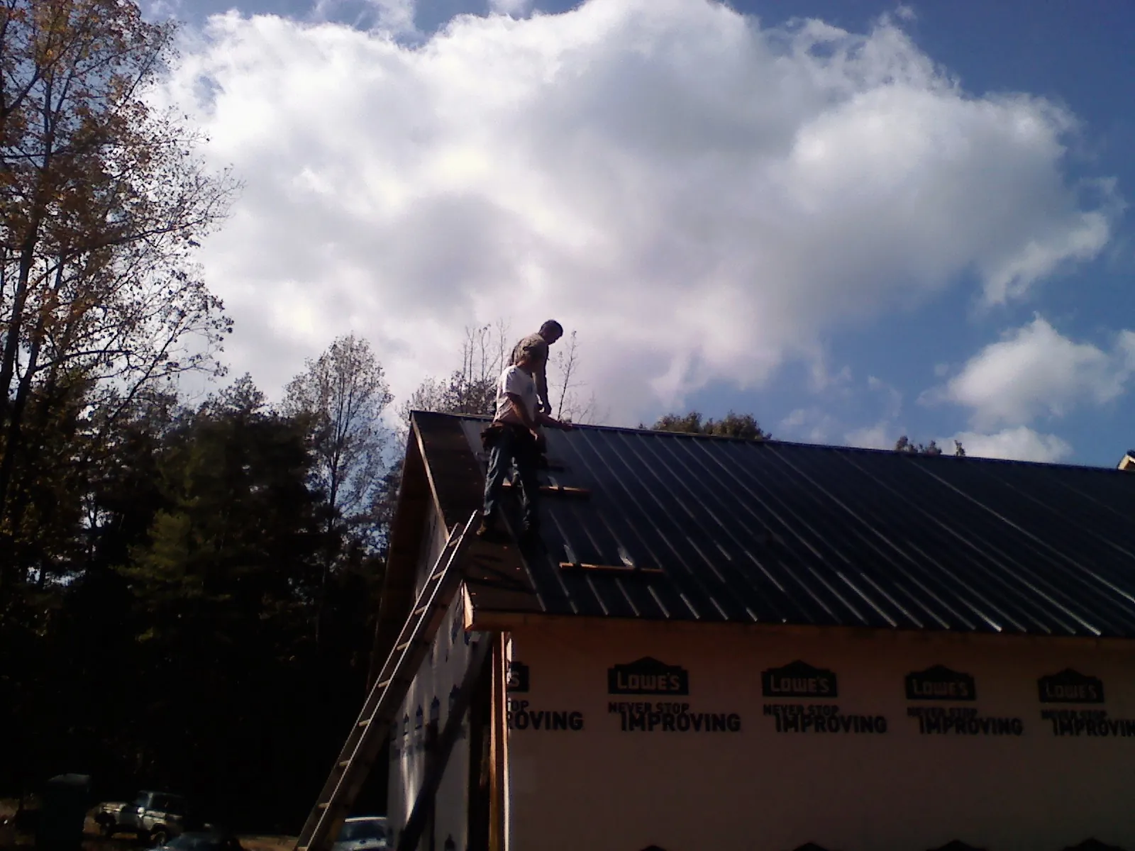 Roofer fastening dark metal panels high against a cloudy sky, from a Roof Inspection job in West Berlin