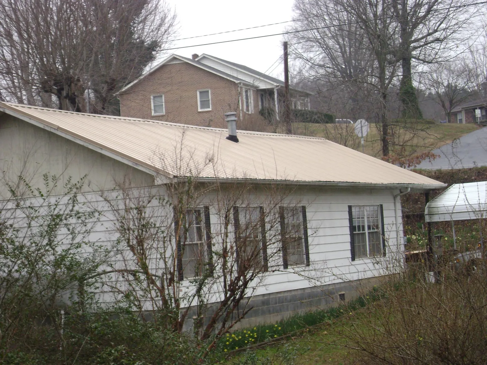 Tan metal roof on a white sided house set into a hillside — Commercial Roofing by Roofing Brothers in West Berlin